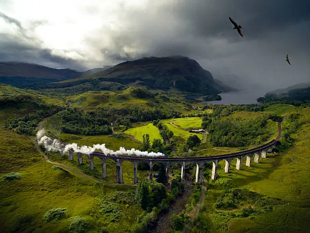 A steam train on a viaduct going through dramatic landscape to Hogwarts, school of Witchcraft and Wizardry