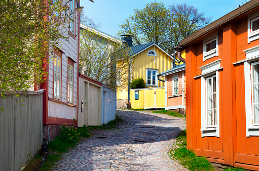 Street view in the old part of the city of Porvoo, Finland,  on a sunny spring day. Wooden empire-style homes painted in yellow, orange and pink surround the cobblestone-paved street. 