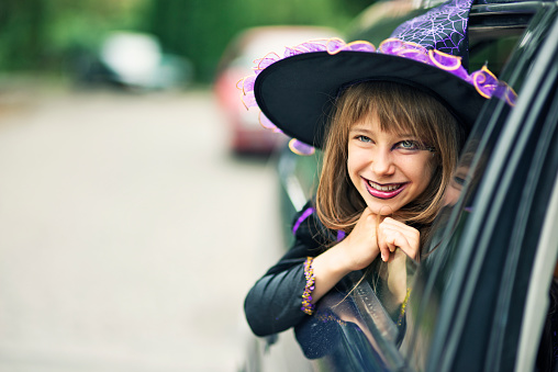 Portrait of a little girl during halloween dressed up as a witch. The girl is aged 9 and is smiling from the car window. Street visible in the background and a lot of nice copy space.
