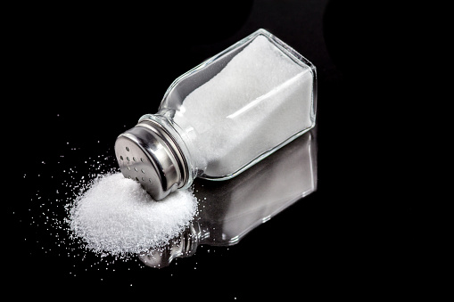Salt shaker with spilled salt on a black background