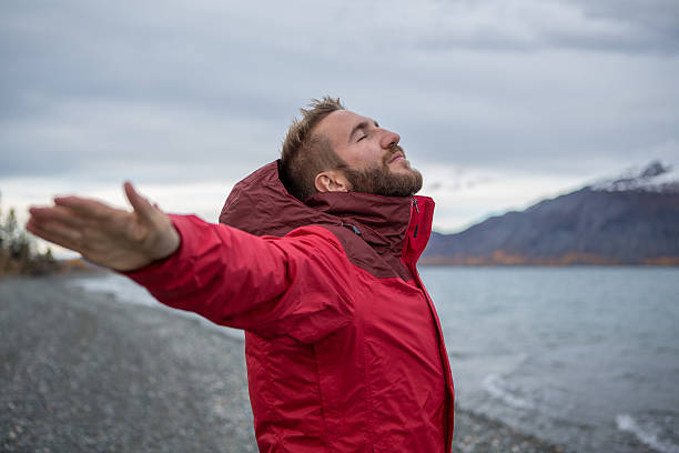 Young cheerful man by the lake enjoying nature. Arms outstretched for positive emotion. 