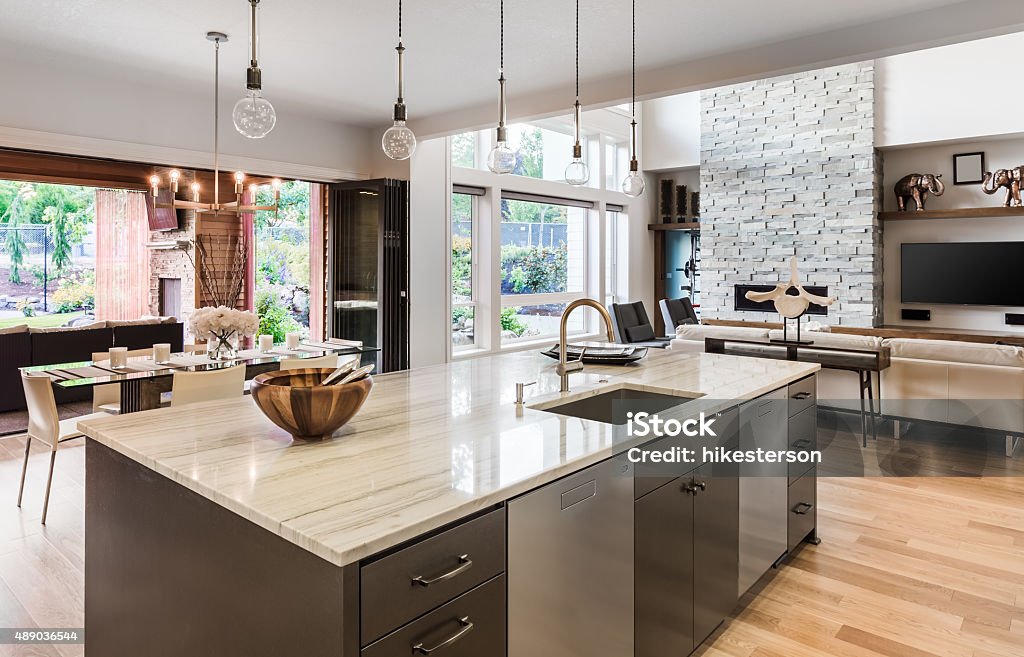 Kitchen in New Luxury Home with Open Floorplan Kitchen with Island, Sink, Cabinets, and Hardwood Floors in New Luxury Home, with View of Living Room, Dining Room, and Outdoor Patio Kitchen Stock Photo