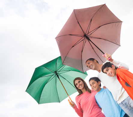 Happy Latin American family outdoors holding umbrellas on a rainy day and smiling