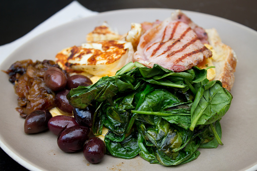 Breakfast with toast, scrambled eggs, spinach, Haloumi cheese, fried ham, Kalamata olives and caramelized onions