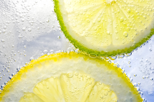 Slices of lemon and lime make bubbles in a glass of icewater.