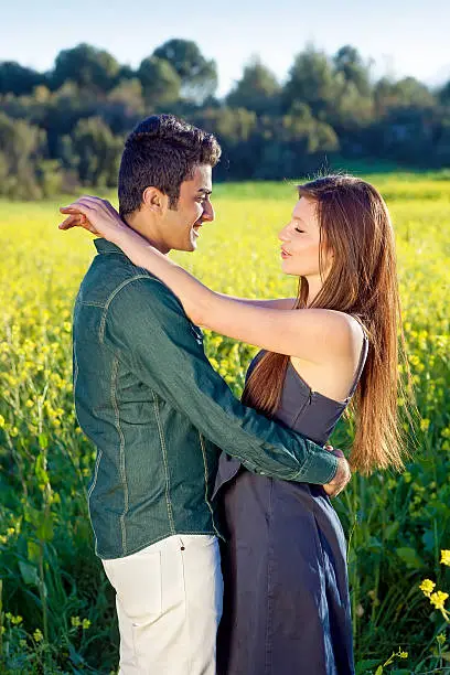 Affectionate young couple in a loving embrace staring tenderly onto each others eyes as they enjoy a sunny day in the country in a field of golden yellow rapeseed.