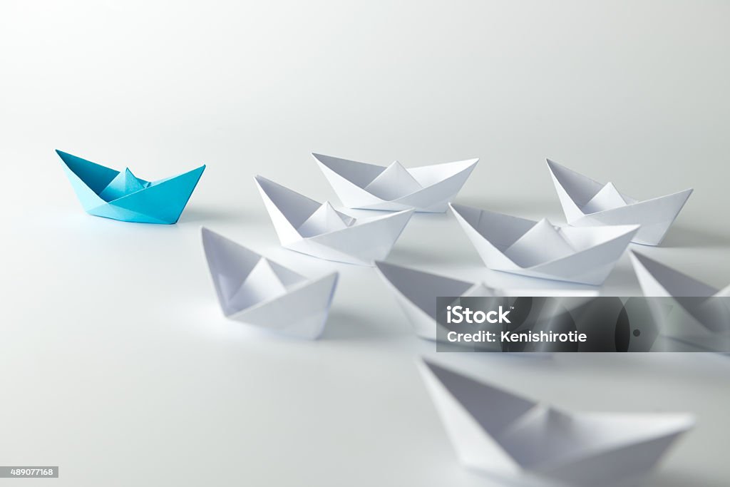 Leadership Leadership concept with blue paper ship leading among white Origami Stock Photo