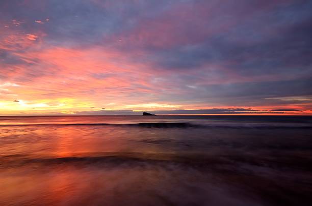 Beach and island of Benidorm Spanish tourist town showing the red colors of the sunrise