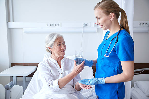nurse giving medicine to senior woman at hospital medicine, age, health care and people concept - nurse giving medication and glass of water to senior woman at hospital ward doctor with water glass stock pictures, royalty-free photos & images