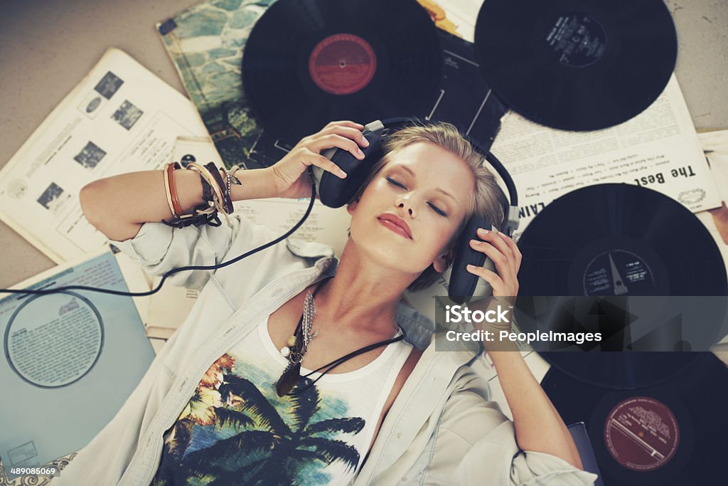 Keep calm and let the music play on A young woman listening to music while lying on her back and surrounded by records Music Stock Photo