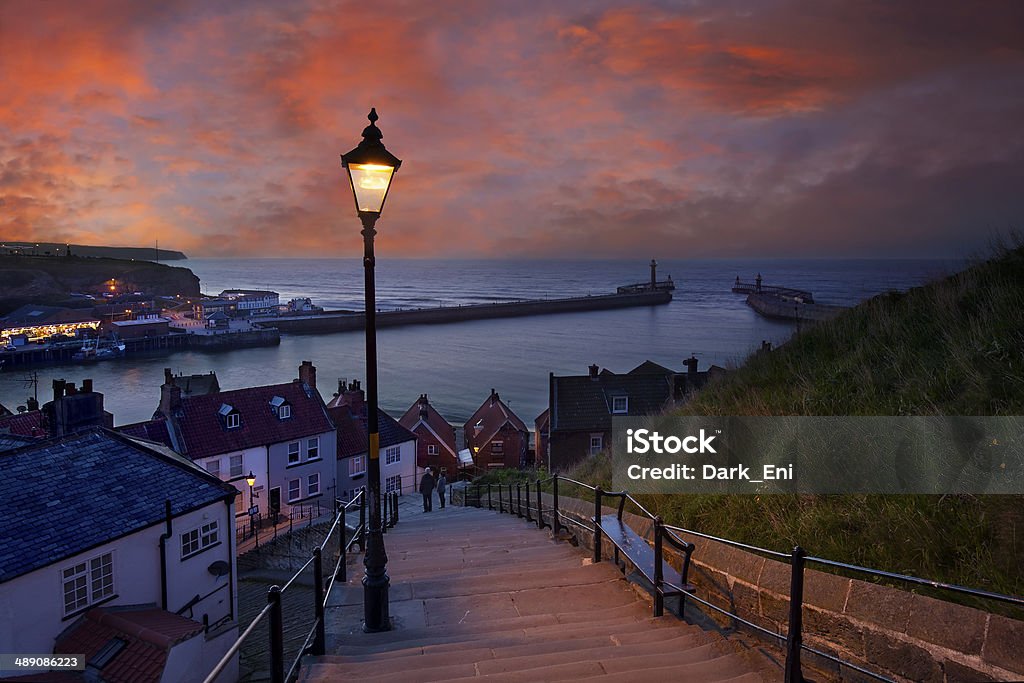 Whitby at dusk - 199 steps leading down from Abbey Whitby is a seaside town, port and civil parish in the Borough of Scarborough and English county of North Yorkshire. Prior to local government reorganizations in the late 1960s it was considered to be part of the North Riding of Yorkshire. Situated on the east coast of Yorkshire at the mouth of the River Esk, Whitby has an established maritime, mineral and tourist heritage. Its East Cliff is home to the ruins of Whitby Abbey, where Caedmon, the earliest recognized English poet, lived. The fishing port emerged during the Middle Ages and developed important herring and whaling fleets, and was (along with the nearby fishing village of Staithes) where Captain Cook learned seamanship. Whitby - North Yorkshire - England Stock Photo