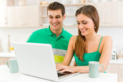 Young happy couple using computer and surfing the net together at home.