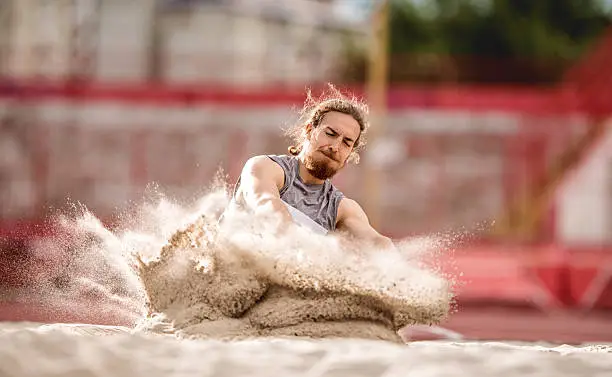 Athlete landing in a sand after a long jump.