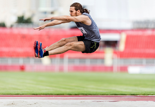 Young man exercising long jump on a stadium.
