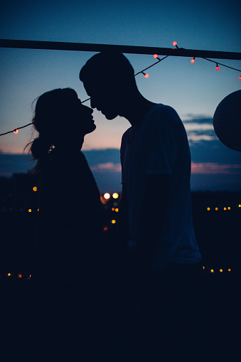 Young couple is kissing on the rooftop of the building, and sharing their love and affection under the evening sky 