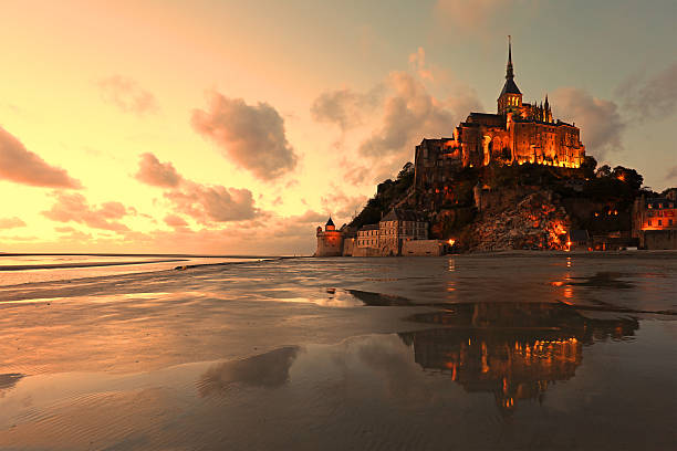 Mont Saint Michel Reflections at Sunset The buildings and the abbey of Mont Saint Michel are lit at sunset on a summer evening. Reflections of this famous island in Normandy, France, can be seen in the low tide water at the bay. mont saint michel photos stock pictures, royalty-free photos & images