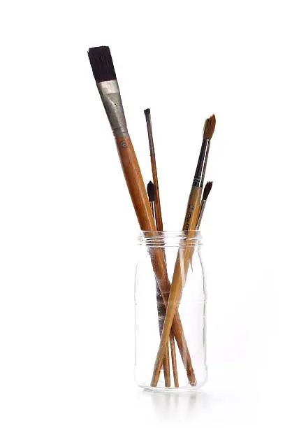 Group of paintbrushes in a glass jar on a white background.