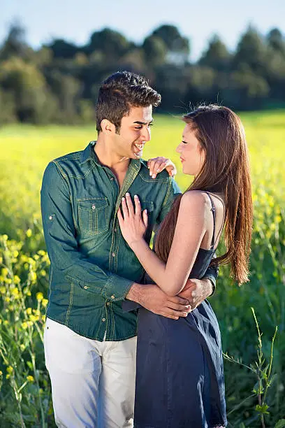 Young couple in love enjoying the countryside standing in an affectionate embrace looking tenderly into each others eyes in a field of yellow rapeseed flowers.