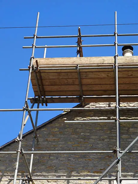 Photo showing some builder's scaffolding poles and planks that are being used to form a wooden platform, so that necessary roofing repairs can be undertaken on this old house.