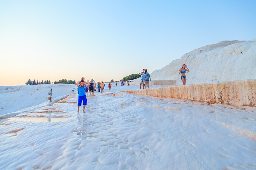 Denizli, Turkey - September 6, 2015: Tourist people are walking on travertine pools and terraces of Pamukkale, Denizli. Pamukkale is a natural site in Denizli Province in southwestern Turkey. The city contains hot springs and travertines, terraces of carbonate minerals left by the flowing water. It is located in Turkey's Inner Aegean region, in the River Menderes valley, which has a temperate climate for most of the year.