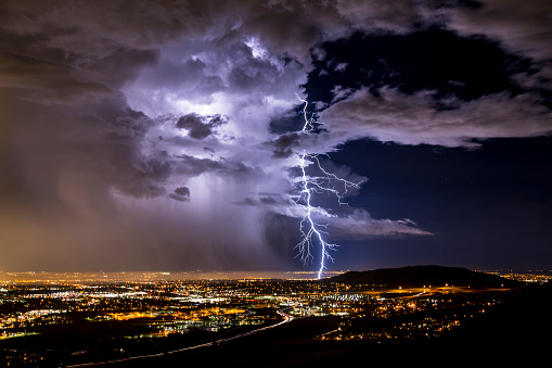 A lightning strike illuminates the clouds over a city on the tailing edge of a storm.