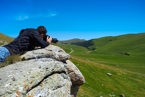 rear view of photographer man capturing images of mountain landscapes.shot taken in Romania, Carpathian mountains.summer season.