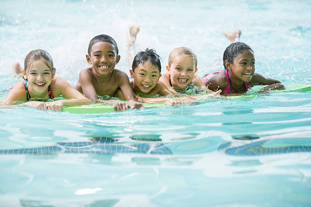 Group Swim Practice A multi-ethnic group of elementary age children are swimming on their kick boards during a swimming lesson. They are smiling and looking at the camera. one piece swimsuit photos stock pictures, royalty-free photos & images