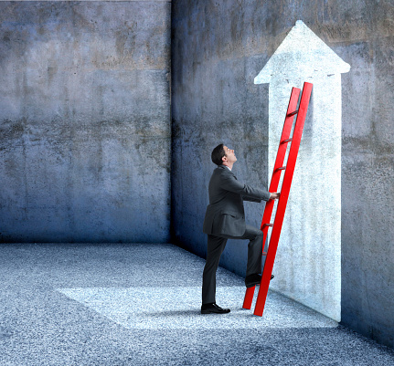 A businessman starting to climb a red ladder leaning up against a cement wall with an arrow on it. There is room for text.