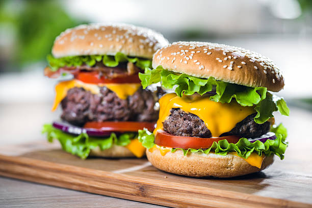 Two Home Made Huge Cheeseburger on oak chopping board Two big homemade delicious cheesburger, with onion, grilled bacon, fresh tomatoes, cheese, and lettuce served on a wooden cutting board cheeseburger stock pictures, royalty-free photos & images
