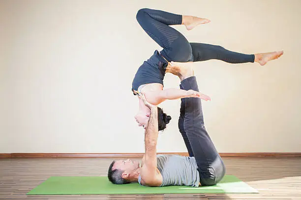 Man and woman doing acro yoga or pair yoga indoor at studio. Concept of couple in sport or family healthy lifestyle