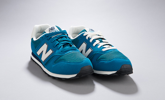 Ankara, Turkey - September 17, 2015: A Pair of blue New Balance shoe with different colored shoelaces over gray background.   