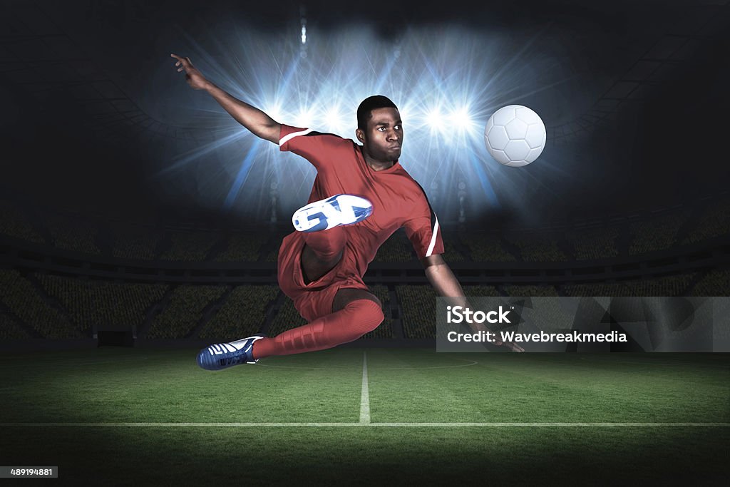 Football player in red kicking Football player in red kicking in a football pitch under spotlights African Ethnicity Stock Photo