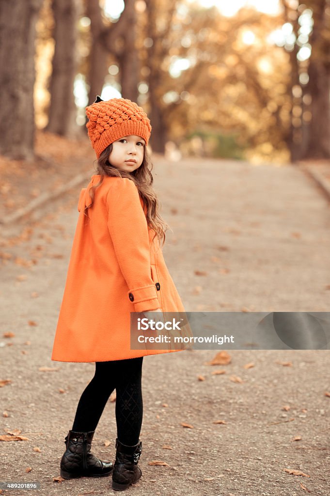 Modern kids Portrait of cute baby girl 6-7 year old posing outdoors. Wearing stylish coat and knitted hat. Walking in park. Childhood. Looking at camera.  Winter Stock Photo