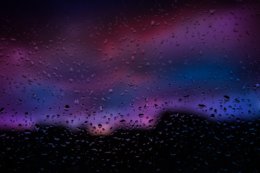 Rain drops on window with beautiful landscape clouds colours in background