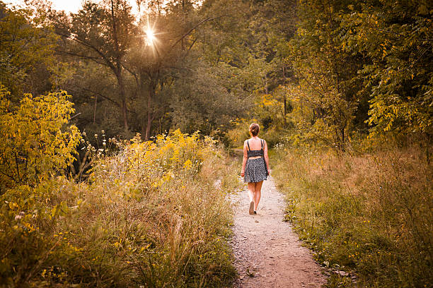 Young woman walking on path in late afternoon summer forest with setting sun
