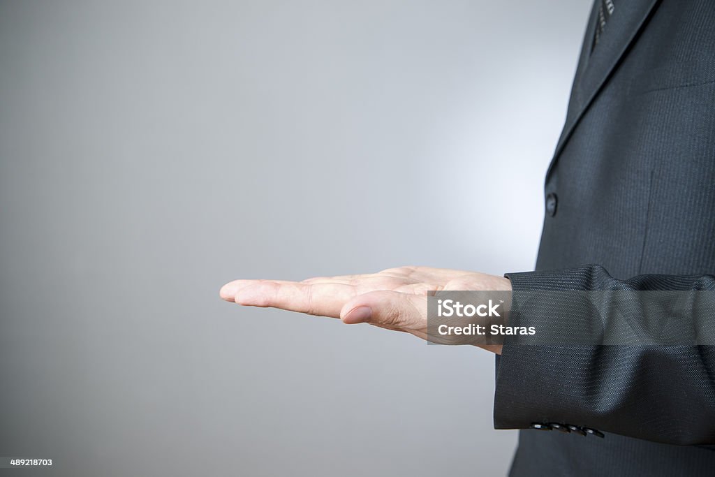 Businessman gesture with his hands Businessman gesture with his hands on gray background. Empty palm. Adult Stock Photo