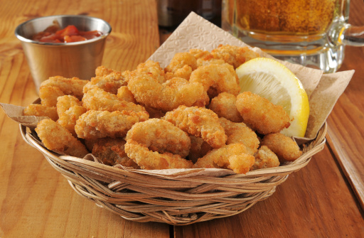 a basket of popcorn shrimp with lemon and cocktail sauce with a mug of beer