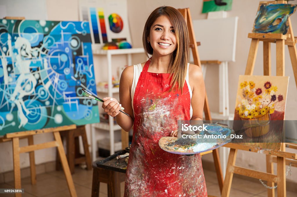 Beautiful female artist in her studio Portrait of a gorgeous female artist working on several art projects on her studio Artist Stock Photo