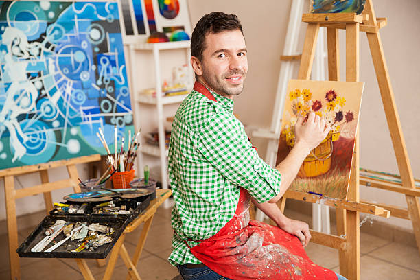 Portrait of a young attractive man working on a painting of flowers and enjoying his work as an artist