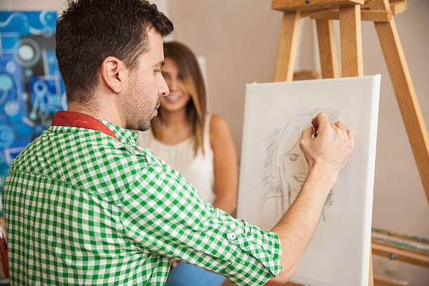 Rear view of a young male artist working on a portrait of a pretty female model in his studio