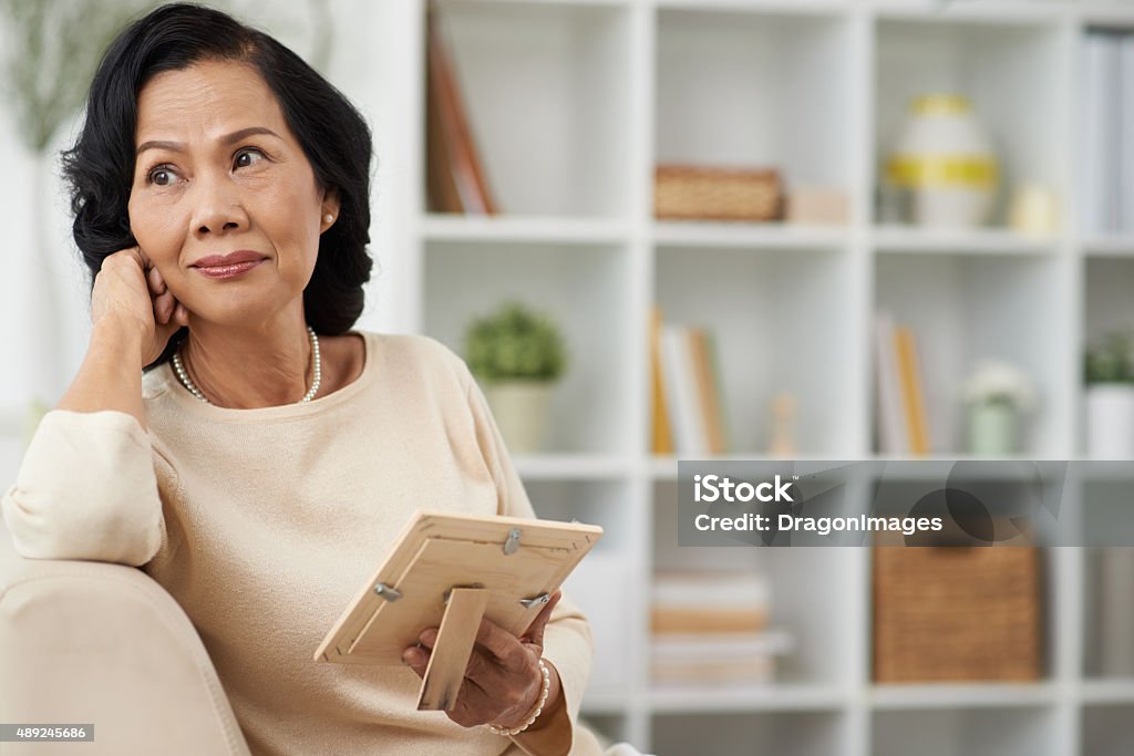 Thoughtful woman Pretty mature woman with a photo in her hands looking thoughtfully to the side Widow Stock Photo