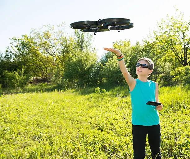 Happy boy playing with flying quadrocopter with camera controlled by smartphone. Kid with quadcopter outdoors.
