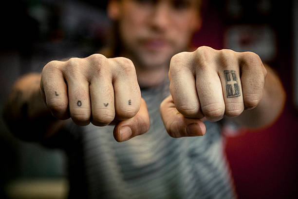 A photo of man's hands with tattoos. Close-up of Love and Cross signs. Tattoo artist is showing art on his fingers at studio.
