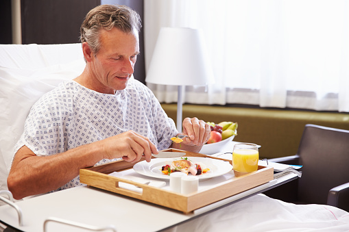 Male Patient In Hospital Bed Eating Meal From Tray
