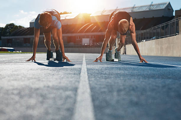 Sprinters at starting blocks ready for race Sprinters at starting blocks ready for race . Athletes at starting position on athletics stadium race track with sun flare. sprint stock pictures, royalty-free photos & images