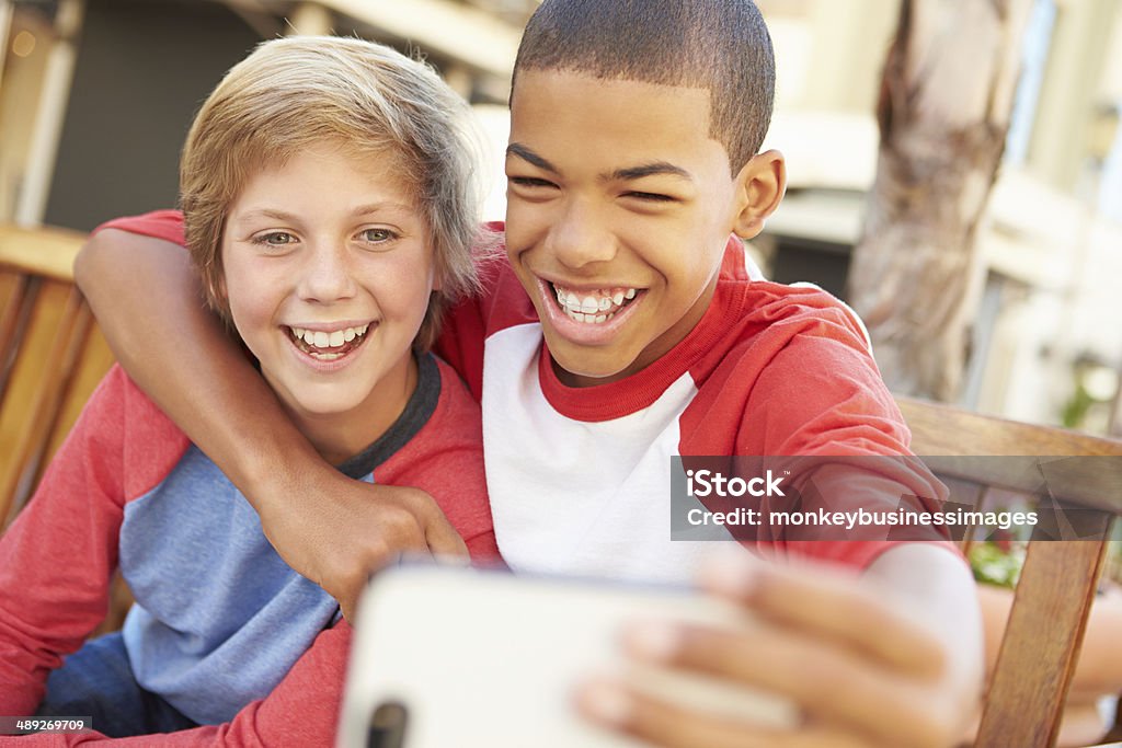 Two Boys Sitting On Bench In Mall Taking Selfie Two Boys Sitting On Bench In Mall Taking Selfie Smiling Teenage Boys Stock Photo