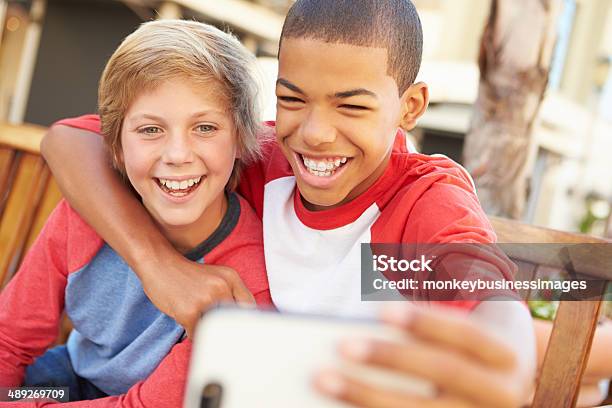 Two Boys Sitting On Bench In Mall Taking Selfie Stock Photo - Download Image Now - Teenage Boys, Friendship, Pre-Adolescent Child