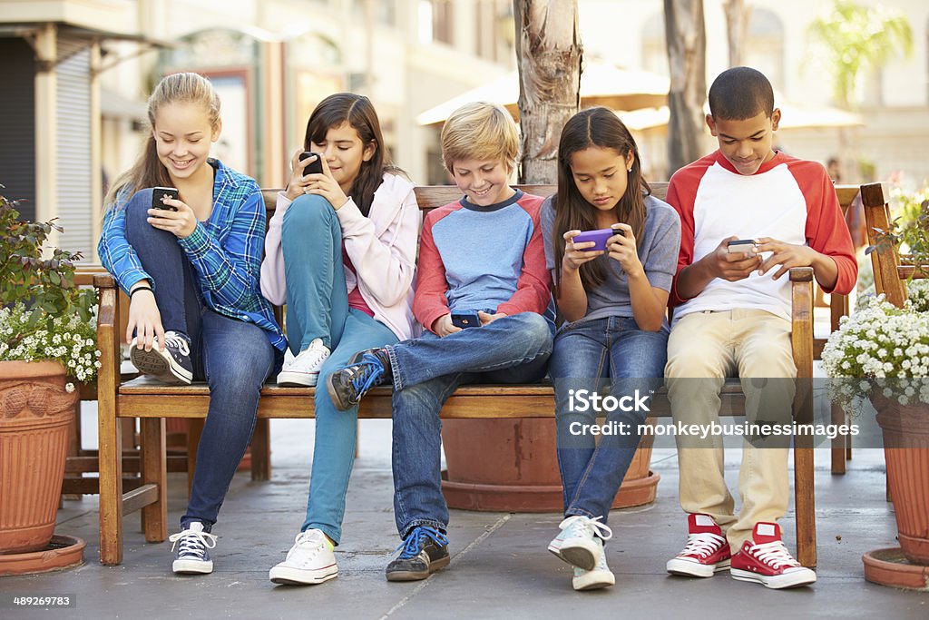 Group Of Children Sitting In Mall Using Mobile Phones Group Of Children Sitting In Mall Using Mobile Phones Smiling Child Stock Photo