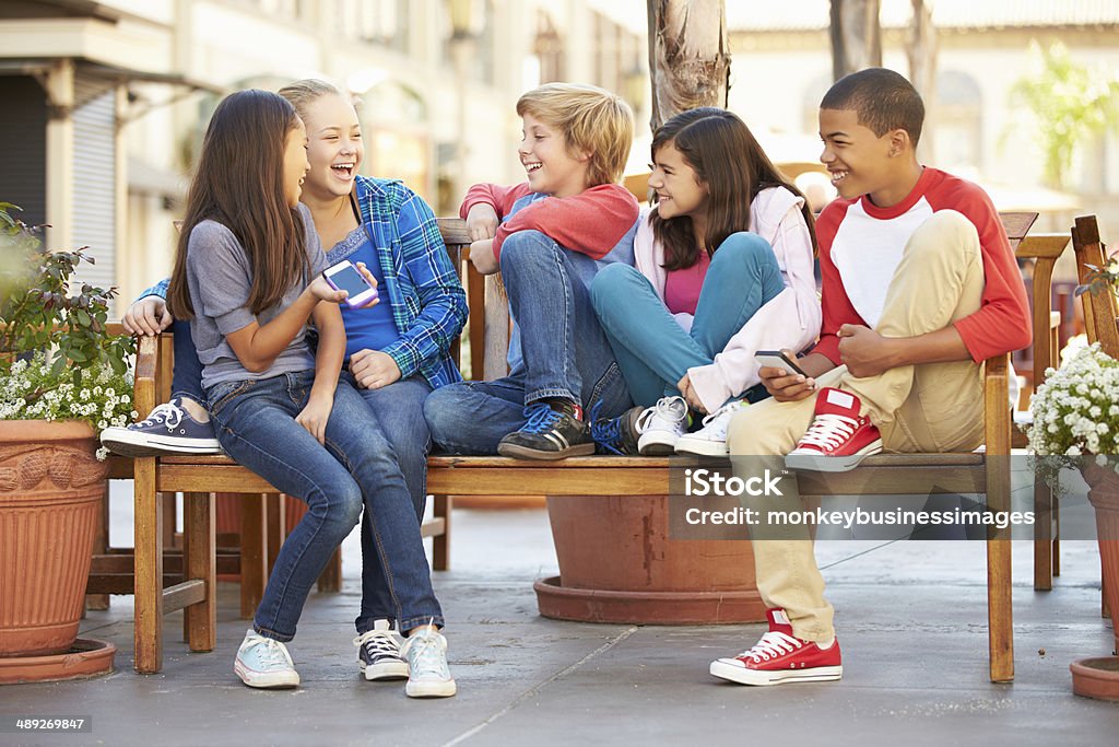 Grupo de niños sentado en el banco en el centro comercial - Foto de stock de Amistad libre de derechos