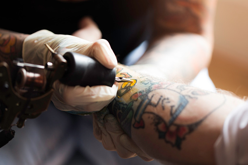 Close up shot of a female tattoo artist using a needle gun to tattoo a man's forearm.